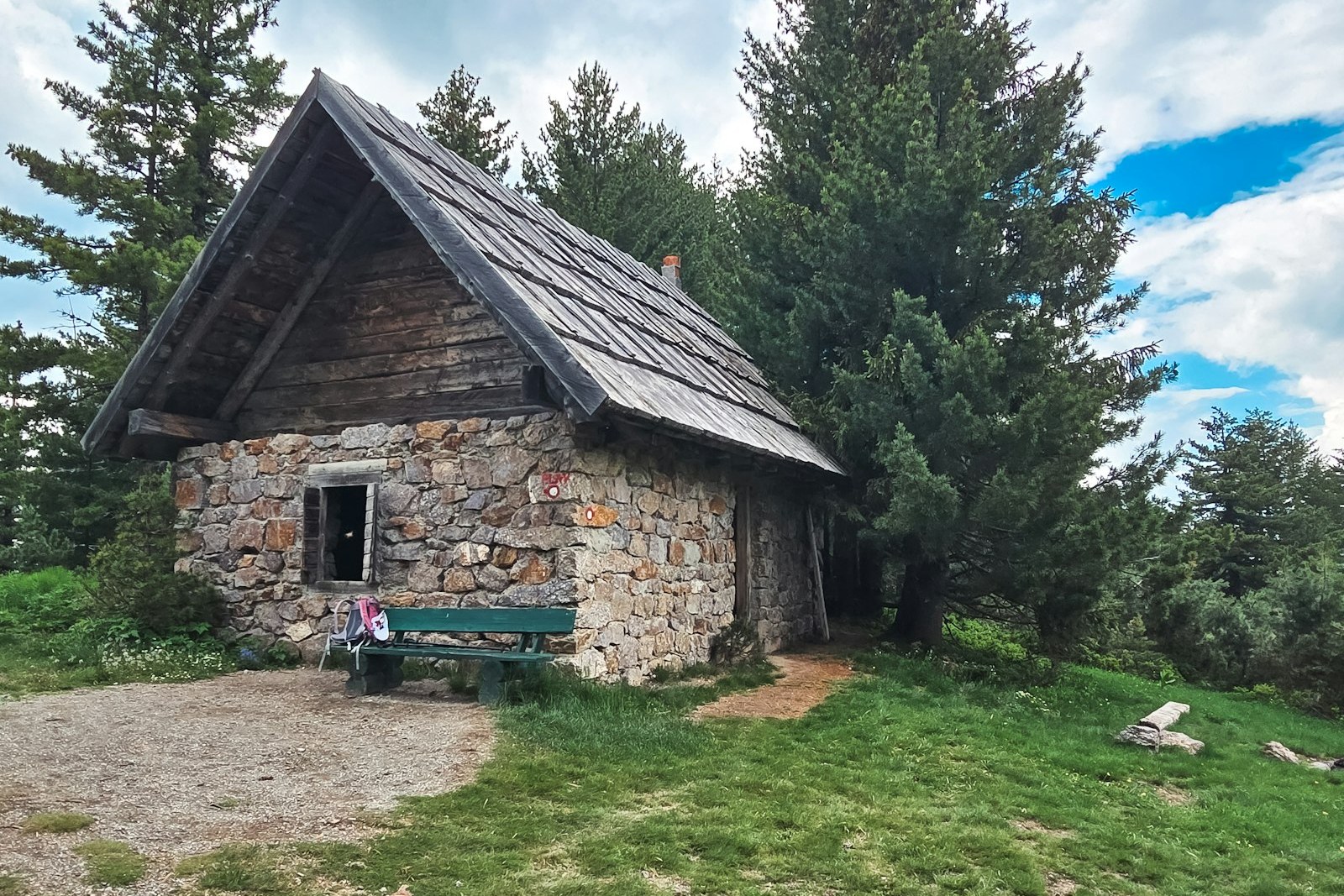 Old stone cabin with wooden roof and green bench, empty of people