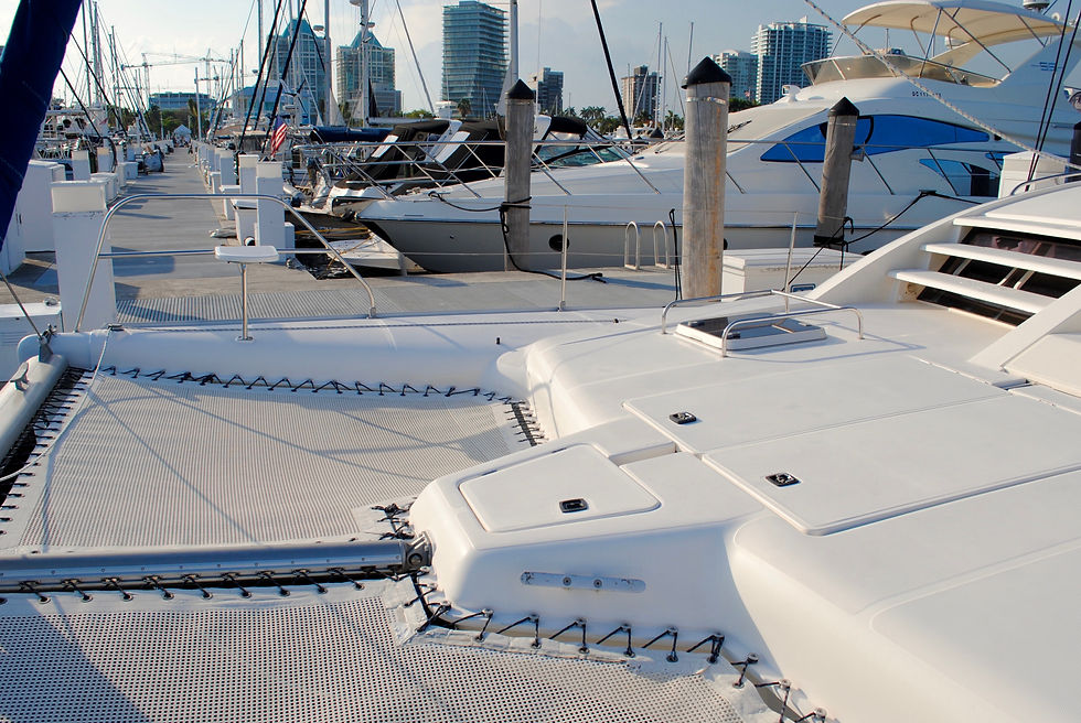 A catamaran's deck in the foreground with rows of moored yachts at Dinner Key Marina in Coconut Grove, Miami, and the downtown Miami skyline visible across the water