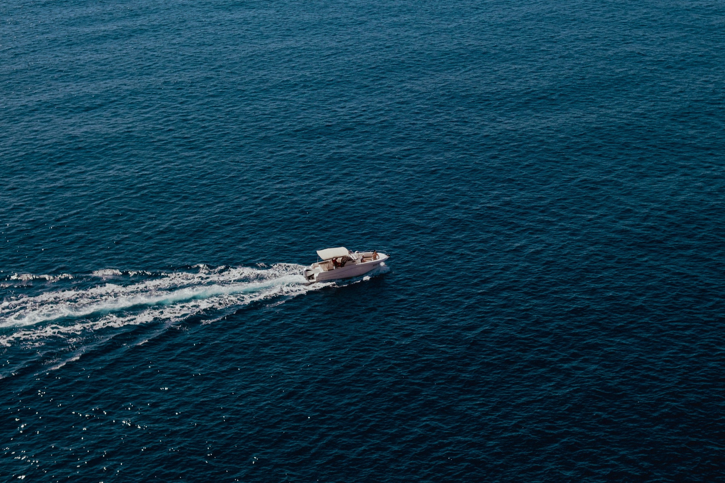 An aerial view of a boat leaving a white wake across deep blue open water