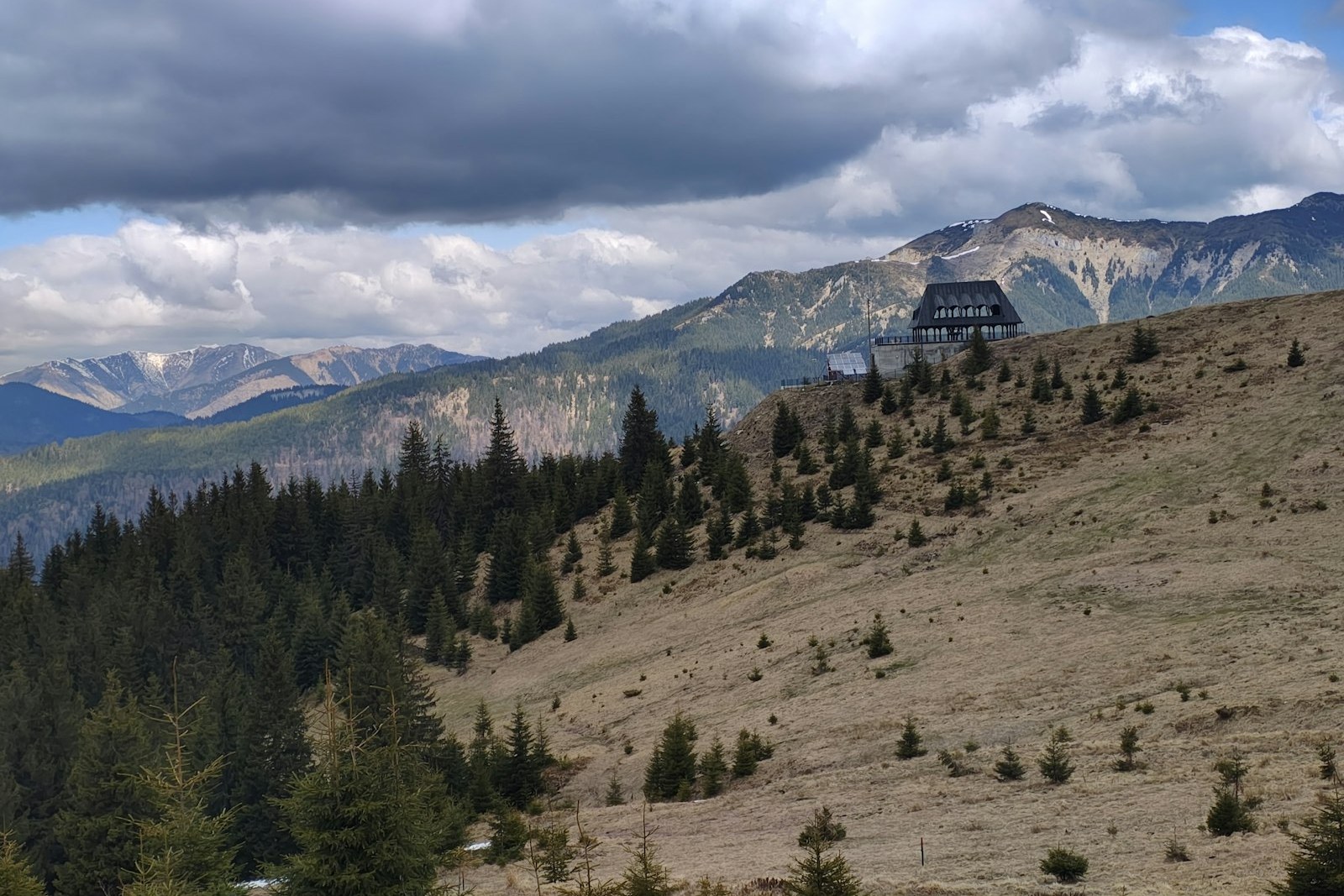 A wooden cabin sits on a grassy mountain slope, empty of people