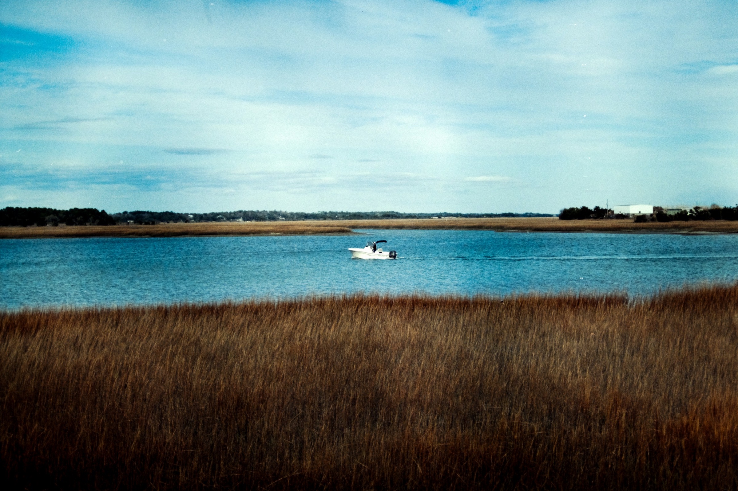 A small boat on a wide blue tidal river with a band of golden marsh grass in the foreground
