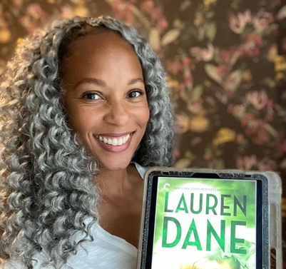 A smiling black woman with grey and black long curly hair is holding a book.