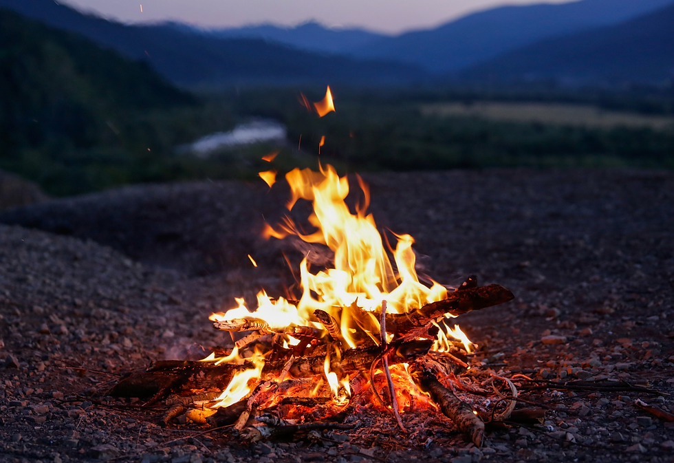 A campfire, set on gravel stone ground, with blurred mountains in background.