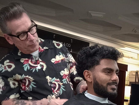 Barber in floral shirt cuts a man’s hair in a modern salon; Apple logo screen in background, calm focused mood.