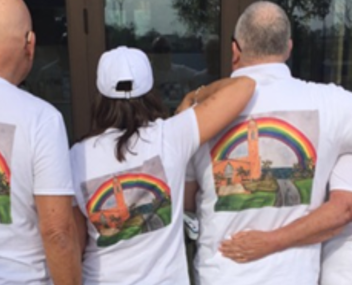 A group of members from GLO stand arm-in-arm wearing t-shirts of a Catholic church and a rainbow.