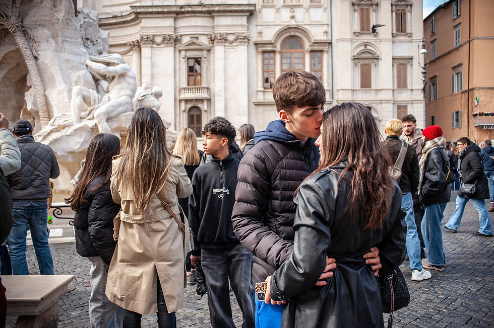 Coppia di giovani si bacia a Piazza Navona a Roma durante il Giubileo 2025, con la Fontana dei Quattro Fiumi e la chiesa di Sant'Agnese in Agone sullo sfondo. Intorno a loro, turisti e pellegrini si muovono tra l'arte barocca e l'atmosfera vibrante della storica piazza romana.