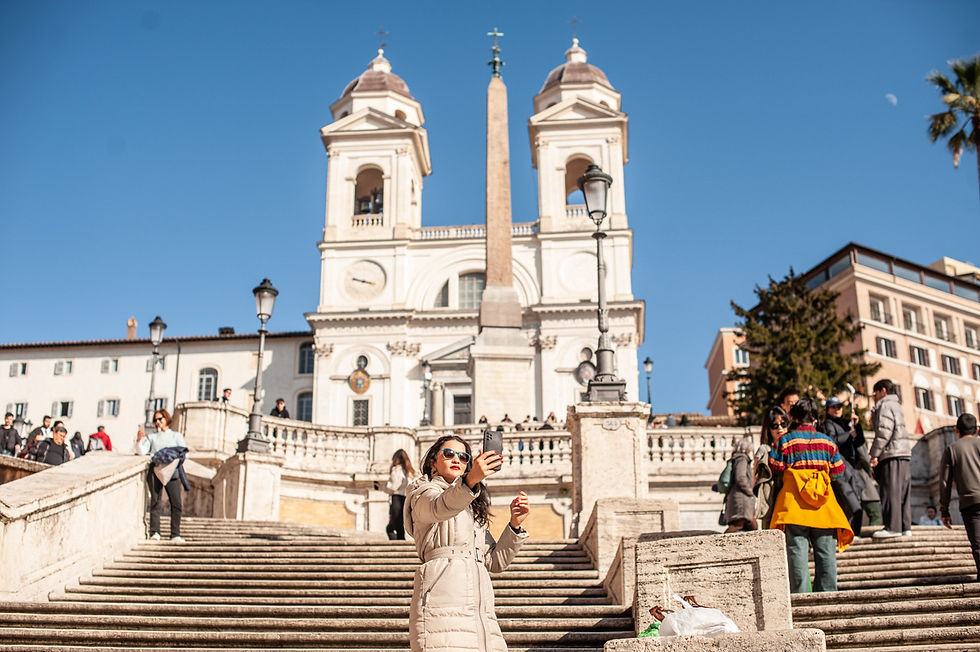 Turisti a Piazza di Spagna a Roma durante il Giubileo 2025. Una donna con occhiali da sole e cappotto chiaro scatta un selfie sulla Scalinata di Trinità dei Monti, con la Chiesa della Trinità dei Monti e l'obelisco sullo sfondo. Il cielo limpido e la folla di visitatori sottolineano l'atmosfera vivace di uno dei luoghi simbolo della città eterna.