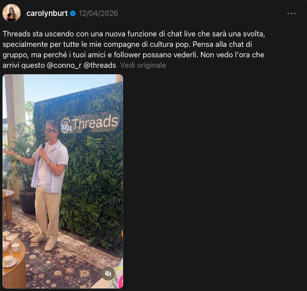 Uomo che parla al microfono vicino a un muro ricoperto di foglie con la scritta "@Threads". Ambiente informale con tavolo, tappeto e piante. Atmosfera luminosa e soleggiata. Threads chat