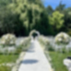 Cerimonia di matrimonio all'aperto con navata bianca, composizioni floreali eleganti e sedute per gli ospiti, progettata da Maison Lumière Wedding Events.