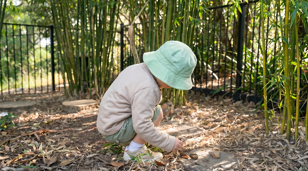 Toddler wearing a soft mint green bucket hat crouching at The Green Elephant on a bright overcast winter morning, absorbed in outdoor play