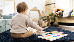 Toddler hands reaching for a board book on the rug