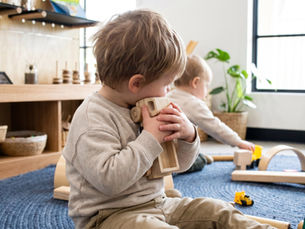 A toddler aged around two clutches a wooden toy truck firmly to their chest while seated on a soft play mat in at The Green Elephant Early Learning Centre