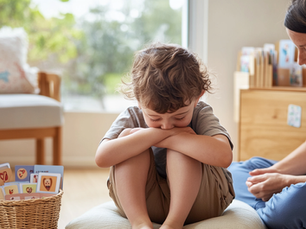 Young child sitting on a cushion hugging their knees while an educator sits quietly beside them