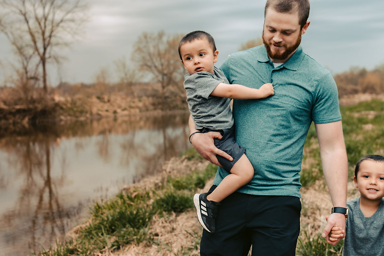 Family photo of a dad walking along a river with his two sons