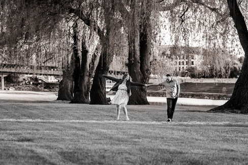 A couple walks through a grassy area lined by weeping willows