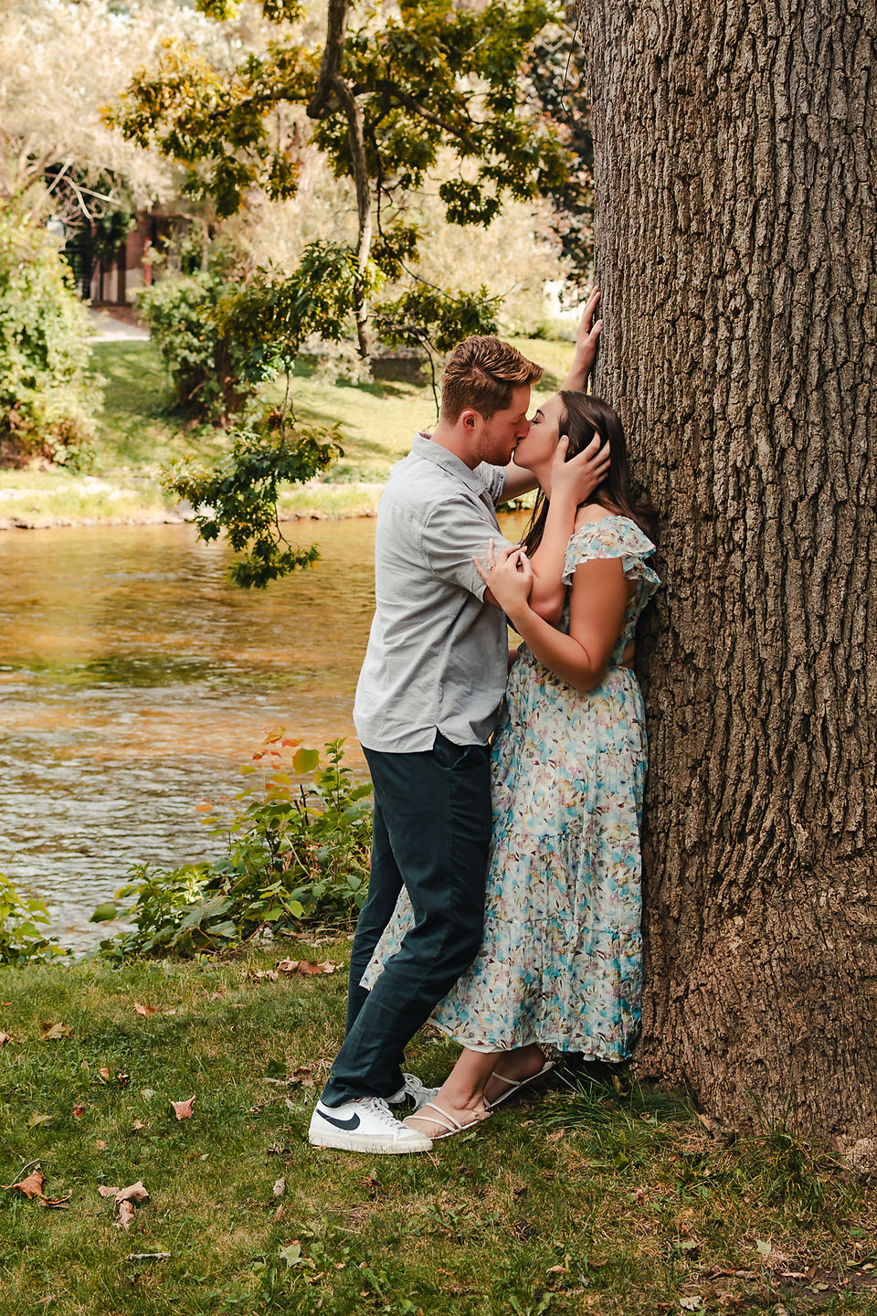 A couple kisses while leaning against a large tree
