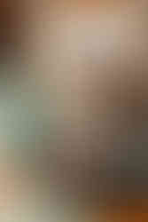 A couple lovingly kisses in front of a kitchen table. A window sits directly behind them.