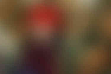 A young girl sits next to small pine trees covered in Christmas lights