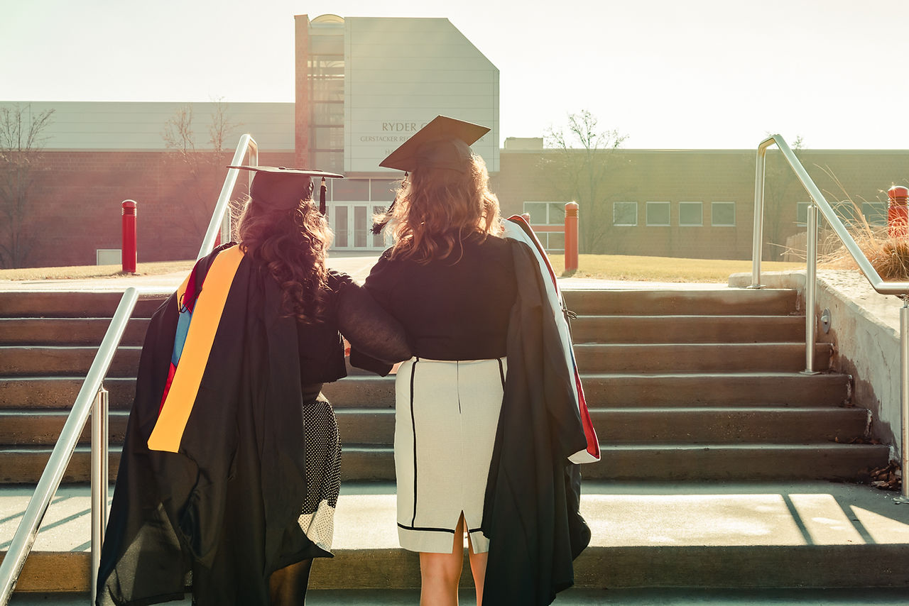 College graduates stand holding their gowns over their shoulders