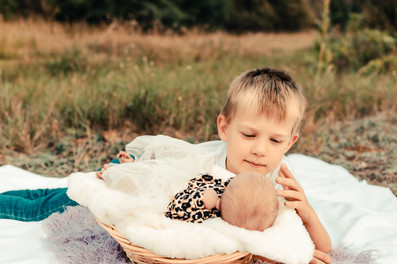 A big brother gently stroking the head of his newborn sister