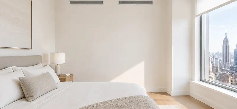 wo slim linear bar grilles set flush near the ceiling of a bright bedroom wall.