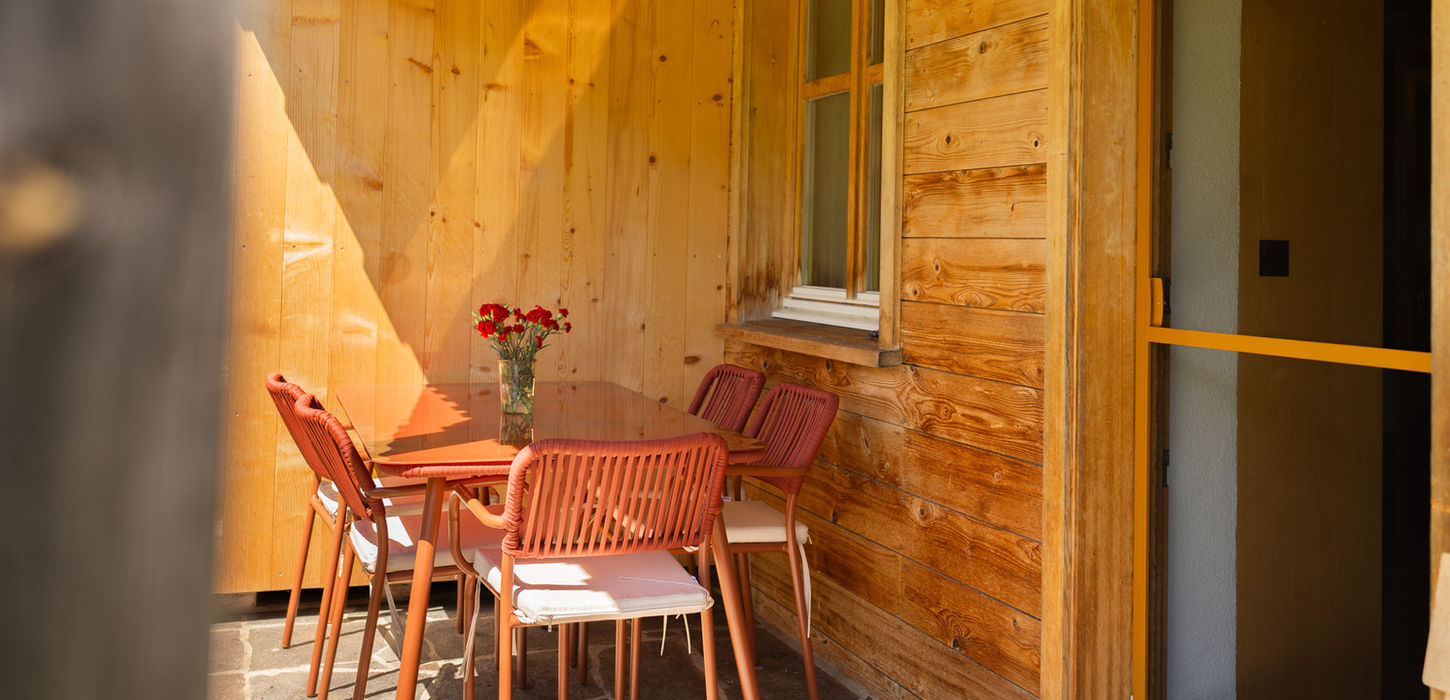 Sonniger Holzterrassen-Essbereich mit rotem Tisch und Stühlen