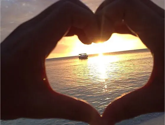 มือเป็นรูปหัวใจกับพระอาทิตย์ตกดิน ท้องทะเล และเรือ