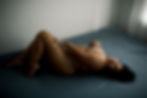 Person lying on a blue bed in a minimalist room with white walls, displaying a relaxed pose. The mood is calm and introspective.