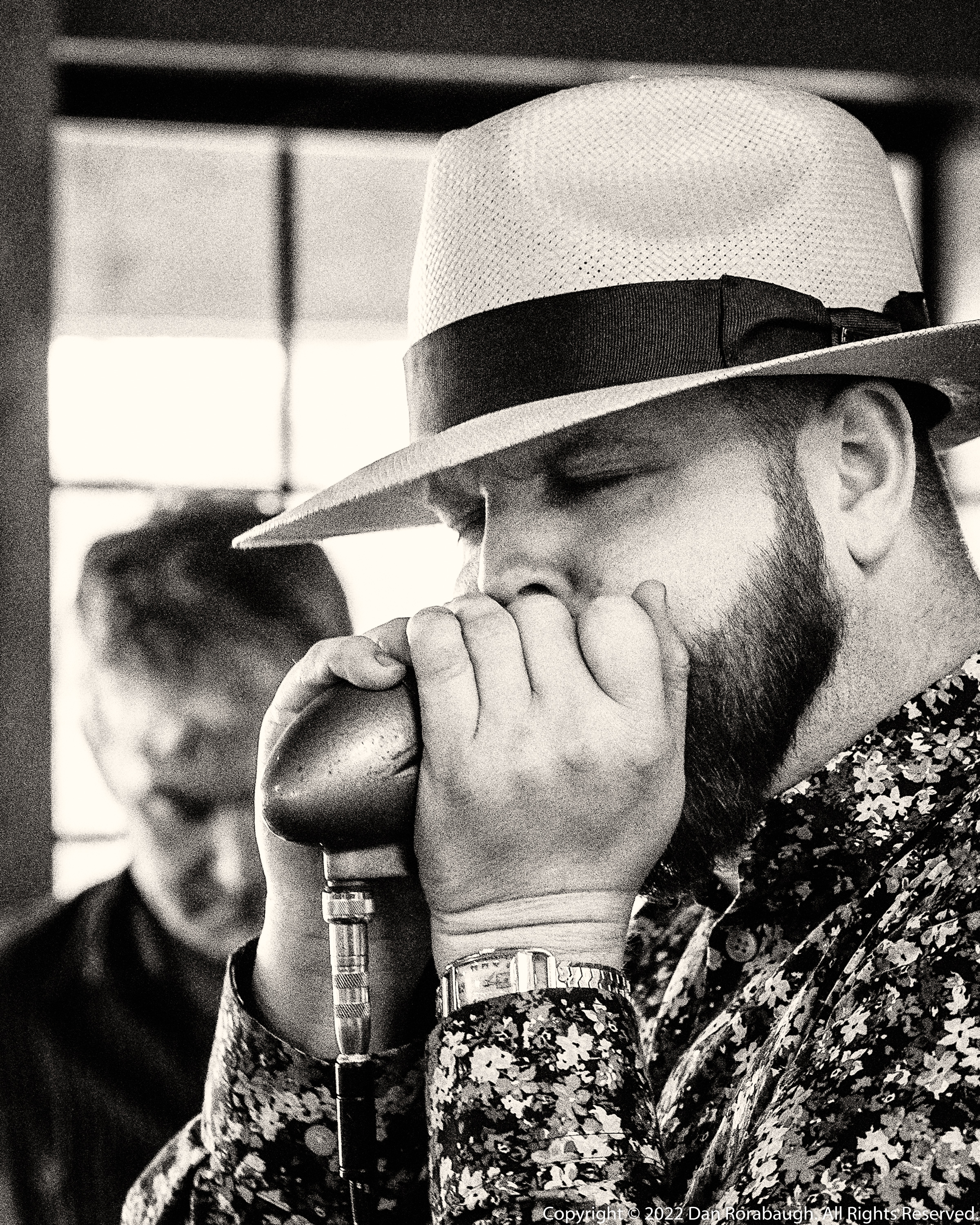 Kyle Rowland playing harmonica in a Panama hat, black and white portrait