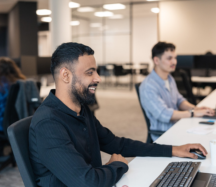 A male member of the FLB team smiles while working on his computer in the office.