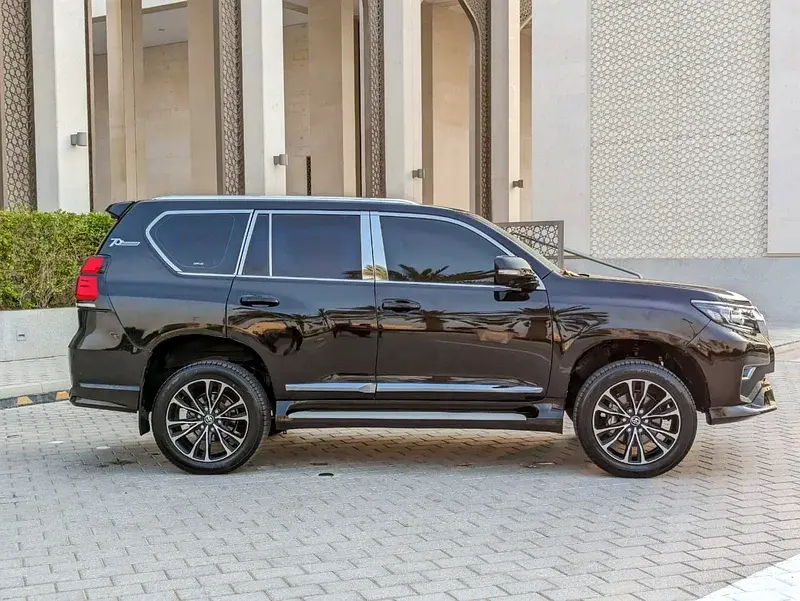 Miniature : Toyota Land Cruiser Prado noir garé devant un bâtiment moderne.