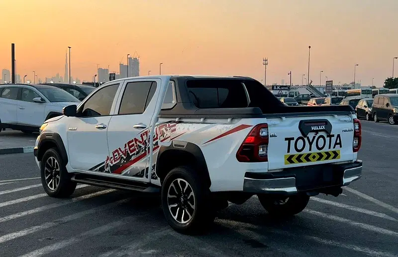 Miniature : Camionnette blanche Toyota Hilux, textes "EVENT" et "TOYOTA", garée au coucher du soleil.