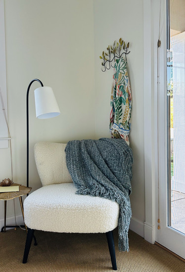 Serene reading nook with boucle accent chair, knit throw, floor lamp, and floral robe on wall hooks.