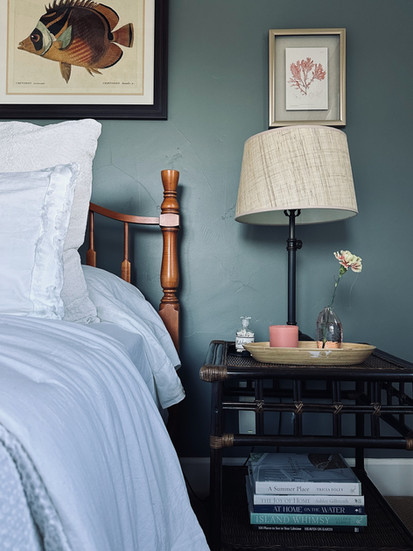 Coastal-inspired bedside vignette with layered textures, vintage artwork, and a curated tray featuring books and florals.