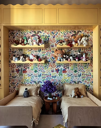 Colorful kids’ room featuring yellow twin beds, bright floral wallpaper, open toy shelves with stuffed animals, and playful, maximalist design details.