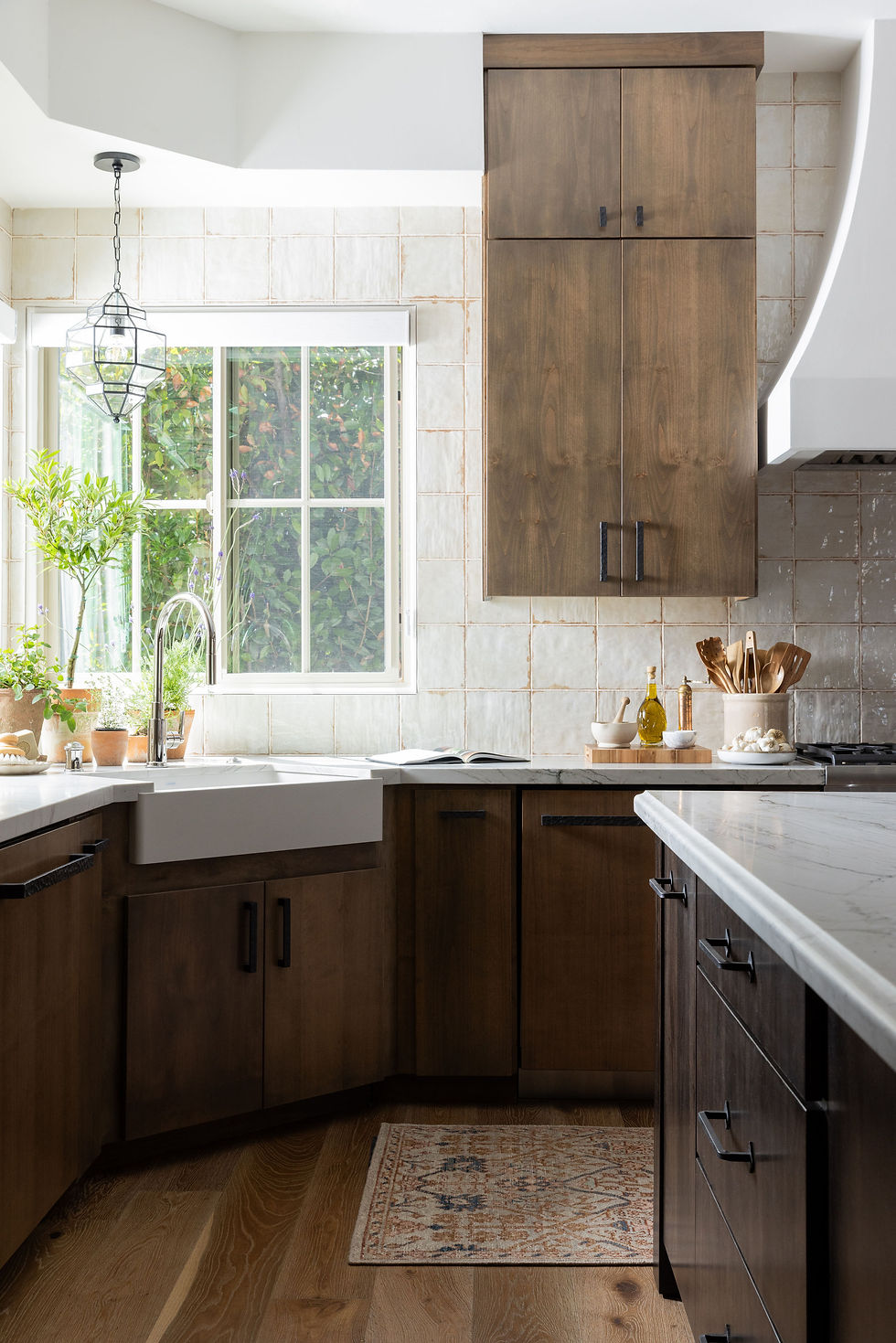 Kitchen featuring layered lighting with a statement pendant over the sink, natural daylight, and warm wood cabinetry creating depth and balance.