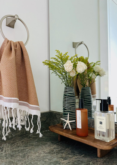 Elevated bathroom vignette with fresh flowers, coastal textures, and luxury hand soap on a wood tray.
