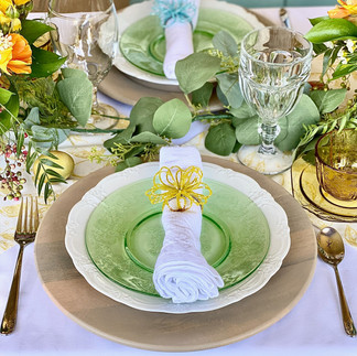 Close-up of an Easter table setting with soft yellow roses, eucalyptus garland, and elegant layered plates in spring colors.