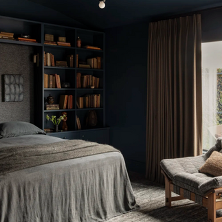 Intimate navy-toned bedroom featuring a custom built-in bookcase, soft linen bedding, and rich textures that create a serene, cocoon-like retreat.