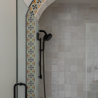 Bathroom shower featuring patterned tile arch detailing, neutral wall tile, and matte black plumbing fixtures.