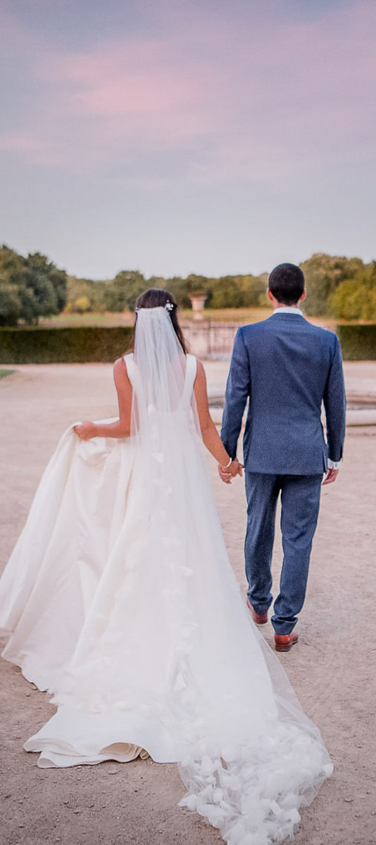 Photographie de mariage en Maine-et-Loire, couple de mariés de dos marchant vers l'horizon à l'heure bleue, séance couple naturelle.