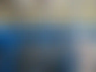 Worker in a hard hat inspects industrial pipes and valves in a factory setting. Blue and yellow structures with metallic surfaces visible.