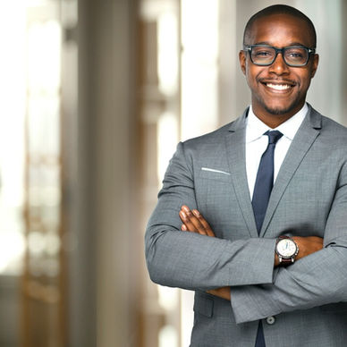An executive crossing their arms and smiling in an office hallway. Two more employees talk behind the executive.