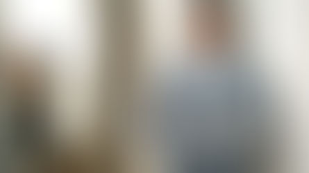 An executive crossing their arms and smiling in an office hallway. Two more employees talk behind the executive.