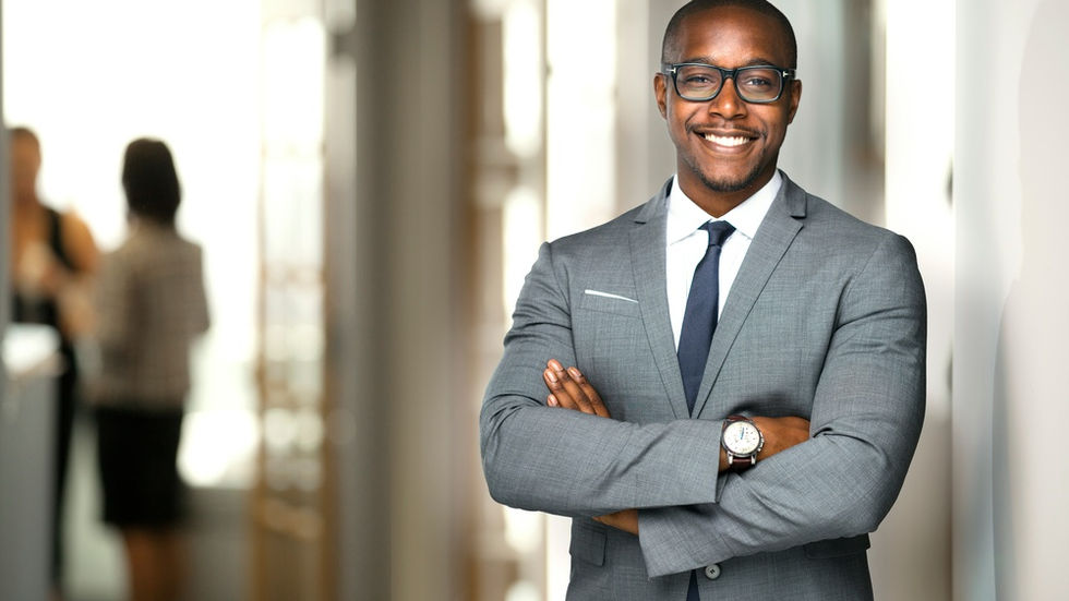 An executive crossing their arms and smiling in an office hallway. Two more employees talk behind the executive.