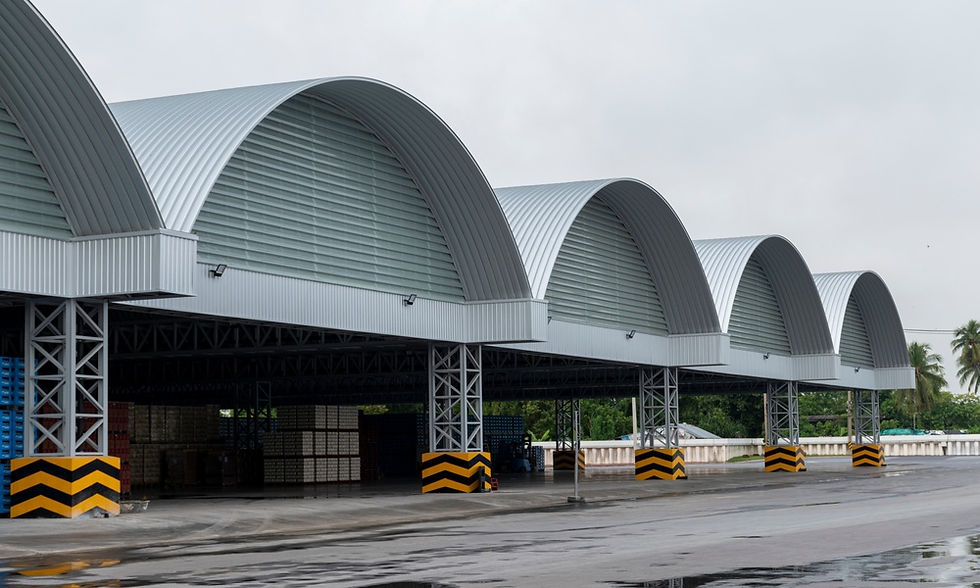 A row of large warehouse bays with curved metal roofs, striped pillars, stacked pallets, and wet pavement.