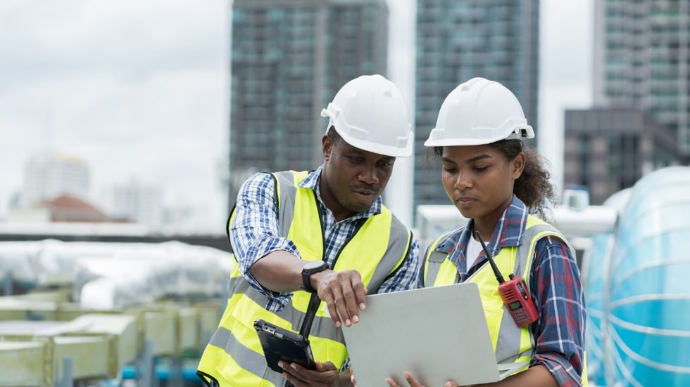 A close-up of two engineers standing outside, looking at a laptop together. They are wearing hard hats and safety vests.