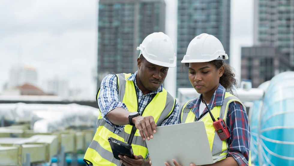 A close-up of two engineers standing outside, looking at a laptop together. They are wearing hard hats and safety vests.