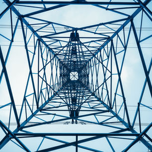 Looking up through a steel transmission tower. Geometric beams form a symmetrical pattern against the open sky.