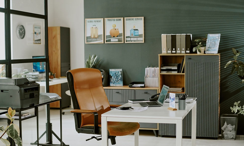 A modern office with organized furniture. Framed art pieces are on the wall while a plant is in the right-hand corner.